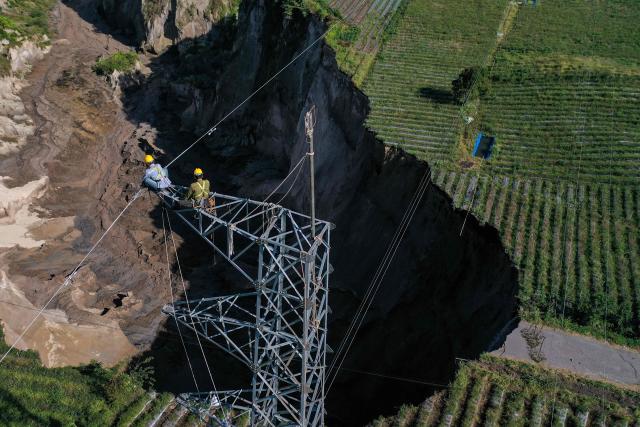 An aerial view shows workers from Indonesia’s state electricity company PLN shutting down operations at a high-voltage transmission tower near a ground collapse owing to landsliding at the Pondok Balik village in Ketol district, Aceh province on February 1, 2026. (Photo by Fadly / AFP)