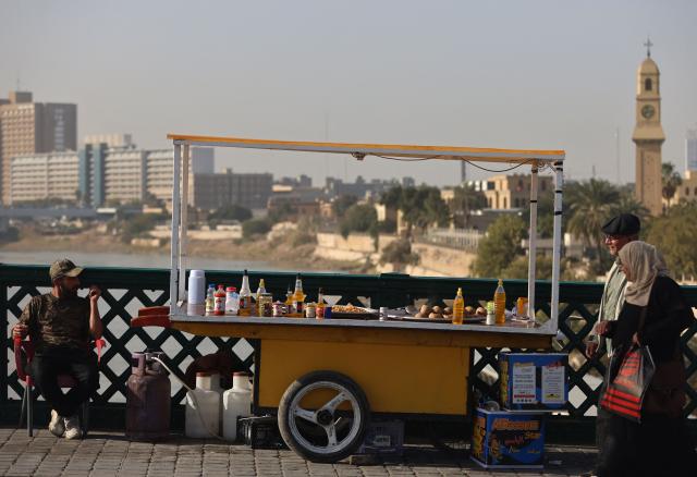 People walk past an Iraqi man selling chickpeas by his cart on Al-Ahrar Bridge over the Tigris River in central Baghdad on February 1, 2026. (Photo by AHMAD AL-RUBAYE / AFP)