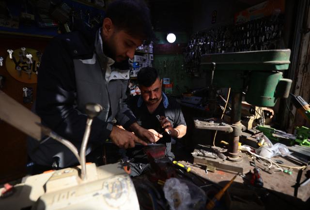 An Iraqi man works with another inside his key-making workshop in the Al-Ukaidad market on Al-Rashid Street in central Baghdad on February 1, 2026. (Photo by AHMAD AL-RUBAYE / AFP)