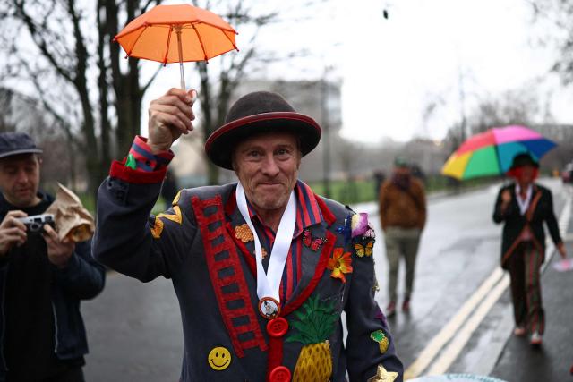 Clowns shelter from the rain under umbrellas on the way to attend the annual Grimaldi Memorial Service at the All Saints Church in east London on February 1, 2026. The annual event is open to clowns from across the world who gather in memory of the legendary Joseph Grimaldi, the "king of clowns", who was a 19th century English stage performer. (Photo by Henry NICHOLLS / AFP)