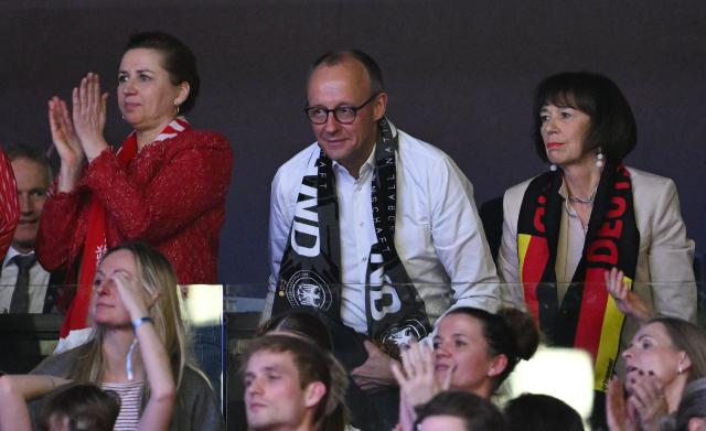 German Chancellor Friedrich Merz (back row C), his wife Charlotte Merz (R) and Danish Prime Minister Mette Frederiksen react as they watch from the stands the Men's EHF Euro 2026 final handball match Denmark vs Germany in Herning, Denmark, on February 1, 2026. (Photo by Jonathan Nackstrand / AFP)