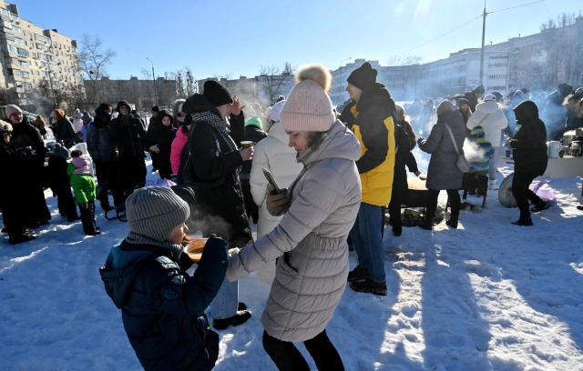 Local residents eat hot soup during an outdoor DJ party in a one of a residential neighbourhood of Kyiv, to lift spirits during mass power outages and central heating on February 1, 2026 amid the Russian invasion of Ukraine. (Photo by Sergei SUPINSKY / AFP)