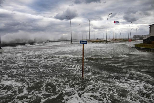 A Cuban flag flutters over the flooded Malecon as waves crash after the arrival of a cold front in Havana on February 1, 2026. (Photo by YAMIL LAGE / AFP)