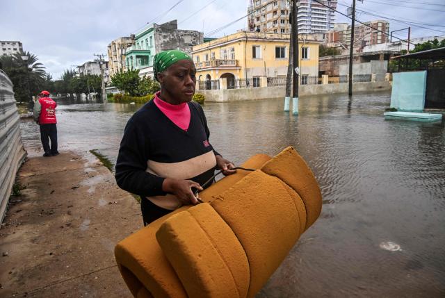 A woman carries a mattress as she walks along a flooded street in Havana after the arrival of a cold front on February 1, 2026. (Photo by YAMIL LAGE / AFP)