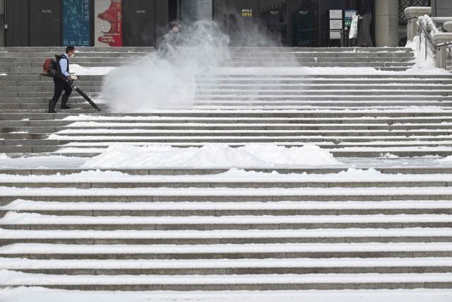 A worker uses a blower to clear snow from the stairs at Gyeongbokgung Palace in Seoul on February 2, 2026. (Photo by Jung Yeon-je / AFP)