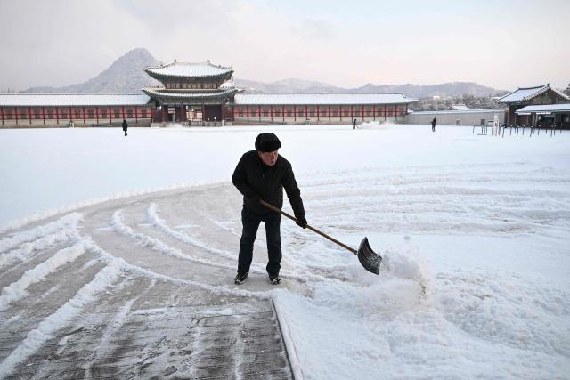 A worker clears snow on the snow-covered grounds of Gyeongbokgung Palace in Seoul on February 2, 2026. (Photo by Jung Yeon-je / AFP)