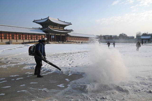 A worker uses a blower to clear snow on the snow-covered grounds of Gyeongbokgung Palace in Seoul on February 2, 2026. (Photo by Jung Yeon-je / AFP)