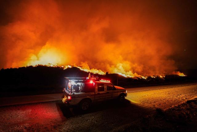Firefighters ride in a vehicle on a road next to a forest fire burning in the mountains of the rural area of Epuyen, in the Patagonian region of Chubut province, Argentina, on February 1, 2026. (Photo by Gonzalo KEOGAN / AFP)