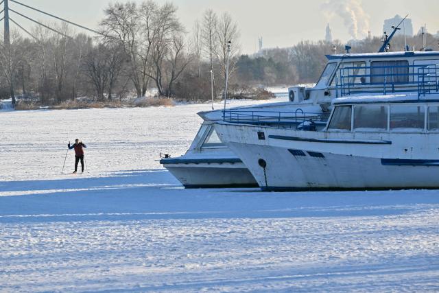 A man skies on the frozen Dnipro River as he passes by moored boats bound by ice during a bitterly frost day in Kyiv on February 1, 2026. (Photo by Sergei SUPINSKY / AFP)