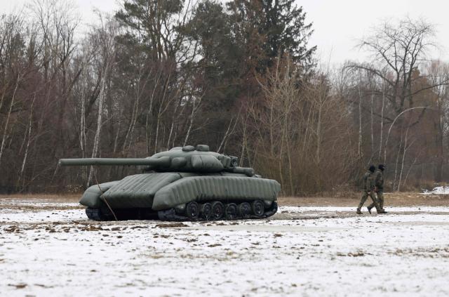 Two soldiers walk past an inflatable mock tank set up for presentation purposes during the visit of the German Defence Minister and Bavarian State Premier (both unseen) at the Innovation Center of the German Armed Forces Bundeswehr in Erding, Bavaria, southern Germany, on February 2, 2026, on the day of the center's inauguration. (Photo by Michaela Stache / AFP)