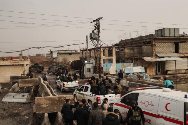 Vehicles of Syrian government internal security forces, followed by an ambulance, drive past Kurdish forces standing at the roadside as they enter the northeastern Syrian city of Hasakeh on February 2, 2026. Syrian government security personnel on February 2, 2026, entered Hasakeh city, a stronghold of Kurdish forces, under an integration deal agreed with the Kurds last week, an AFP team reported. The two sides reached a comprehensive agreement on January 30 to gradually integrate the Kurds' military and civilian institutions into the state, after Kurdish forces ceded territory to advancing government troops in recent weeks after months of tensions and sporadic clashes. (Photo by Delil SOULEIMAN / AFP)