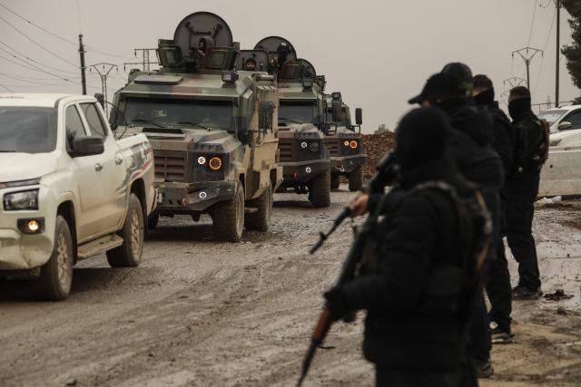 Kurdish forces stand at the roadside as vehicles of the Syrian government internal security forces enter the northeastern Syrian city of Hasakeh on February 2, 2026. Syrian government security personnel on February 2, 2026, entered Hasakeh city, a stronghold of Kurdish forces, under an integration deal agreed with the Kurds last week, an AFP team reported. The two sides reached a comprehensive agreement on January 30 to gradually integrate the Kurds' military and civilian institutions into the state, after Kurdish forces ceded territory to advancing government troops in recent weeks after months of tensions and sporadic clashes. (Photo by Delil SOULEIMAN / AFP)