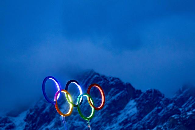 The illuminated Olympic rings are seen on the roof the Olympic stadium with mountain peaks behind it in Cortina d'Ampezzo, northern Italy prior to the Milano Cortina 2026 Olympic Games, on February 2, 2026. (Photo by Odd ANDERSEN / AFP)