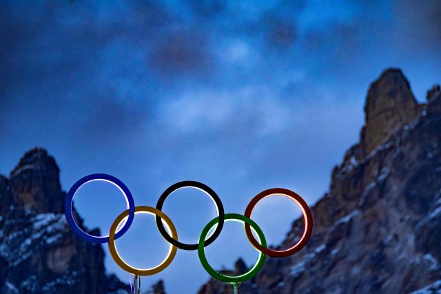 TOPSHOT - The illuminated Olympic rings are seen on the roof the Olympic stadium with mountain peaks behind it in Cortina d'Ampezzo, northern Italy prior to the Milano Cortina 2026 Olympic Games, on February 2, 2026. (Photo by Odd ANDERSEN / AFP)