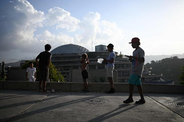 Youngsters fly a kite in the San Agustin neighborhood while in the background is seen the 'El Helicoide' building, the headquarters of the Bolivarian National Intelligence Service (SEBIN), in Caracas on February 2, 2026. On February 2 Washington's new top diplomat in Venezuela said that in a meeting with the country's interim president she addressed the issue of a transition after the ouster of Nicolas Maduro. (Photo by Federico PARRA / AFP)