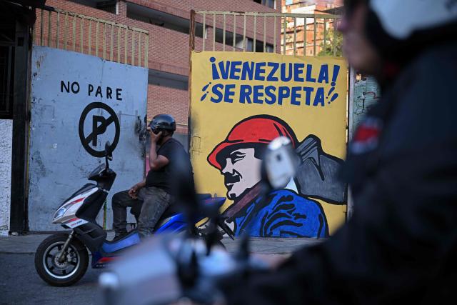 A motorcyclist stands next to a mural depicting ousted President Nicolas Maduro that reads in Spanish “Venezuela is Respected” in Caracas on February 2, 2026. On February 2 Washington's new top diplomat in Venezuela said that in a meeting with the country's interim president she addressed the issue of a transition after the ouster of Nicolas Maduro. (Photo by Federico PARRA / AFP)
