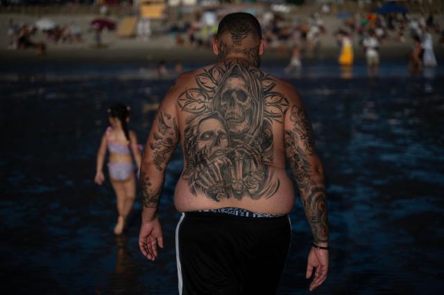 A man with a tattooed back walks at the beach as believers offer tribute to Iemanja, the Goddess of the Sea of the Afro-American religion Umbanda, at Ramirez Beach in Montevideo on February 2, 2026. (Photo by Eitan ABRAMOVICH / AFP)