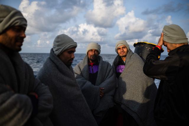 (FILES) Bangladeshi migrants wrapped in blankets stand on the aft deck of the rescue ship "Ocean Viking," operated by the NGO SOS Mediterranee, as it sails in the Mediterranean Sea toward the designated port of disembarkation in Palermo, southern Italy, on January 18, 2026. Nearly six months after coming under fire off the coast of Libya, the "Ocean Viking", an ambulance ship chartered by SOS Mediterranee, has returned to sea for the first time in recent weeks, rescuing more than 120 migrants in a sometimes tense context. (Photo by Sameer Al-DOUMY / AFP)