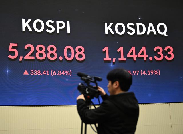 A cameraman films in front of an electronic screen showing South Korea's benchmark stock index Kospi (L) and the Korean Securities Dealers Automated Quotations (KOSDAQ) at the Korea Exchange in Seoul on February 3, 2026. Japanese and South Korean stocks rallied on February 3, to claw back much of the previous day's huge losses suffered in an Asia-wide rout. (Photo by Jung Yeon-je / AFP)