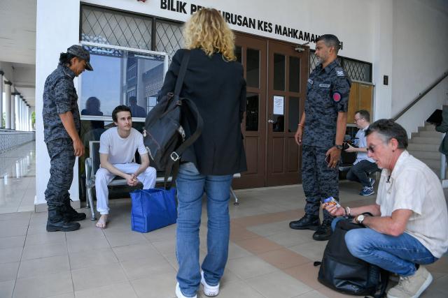 French national Tom Felix (2nd L) sits next to Malaysian immigration officers as his parents Jean Luc Felix (R) and Sylvie Felix (C) look on after he was acquitted on eight drug-related charges at the High Court in Alor Setar on February 3, 2026. A Malaysian court acquitted on February 3 a French national facing the death penalty of eight drug-related charges, freeing him after nearly two and a half years in detention. (Photo by Hakim Mustapha / AFP)