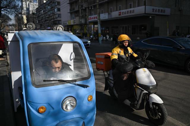 Delivery workers are seen on a street in Beijing on February 3, 2026. (Photo by Pedro PARDO / AFP)