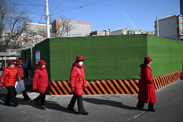 Women wearing red jackets walk along a street in Beijing on February 3, 2026. (Photo by Pedro PARDO / AFP)