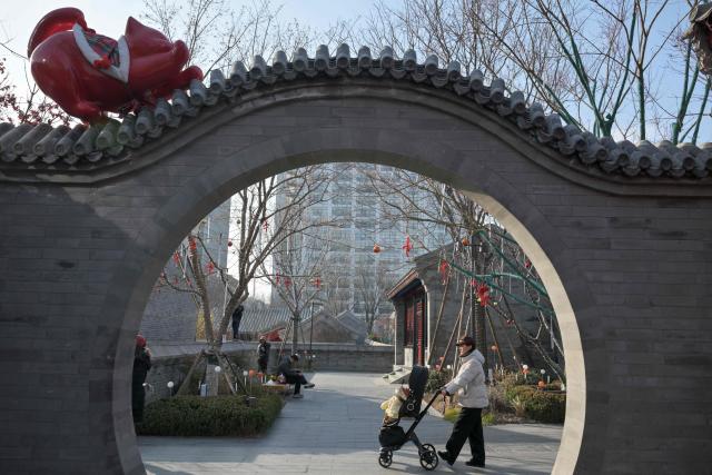 A woman pushes a child on a stroller past an archway with an installation of a cat stretching at the Zhonghai Daji Alley shopping centre in Beijing on February 3, 2026. (Photo by ADEK BERRY / AFP)