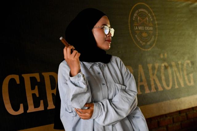 A woman samples a homemade cigar in Montasik, Aceh province on February 3, 2026. (Photo by CHAIDEER MAHYUDDIN / AFP)