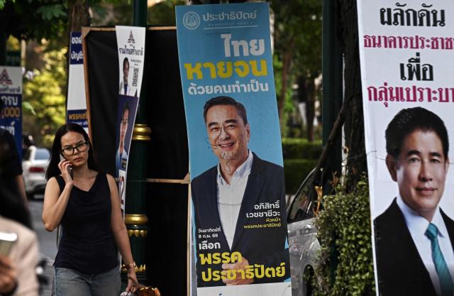 People walk past a defiled campaign poster of Democrat Party's prime ministerial candidate Abhisit Vejjajiva (C) before the February 8 general election in Bangkok on February 3, 2026. (Photo by Lillian SUWANRUMPHA / AFP)