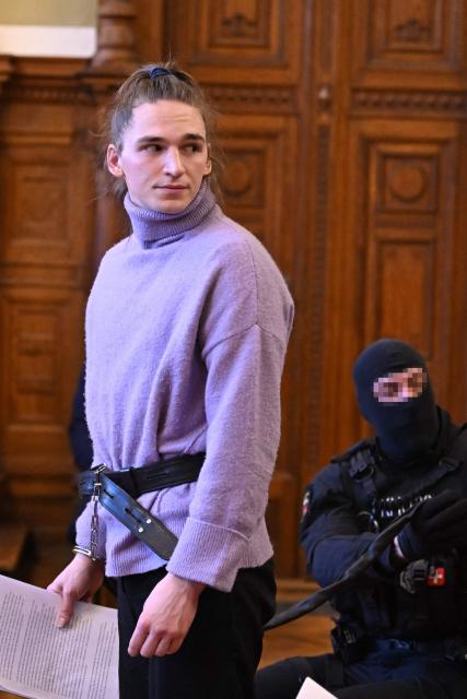 (FILES) The defendant, German anti-fascist activist Maja T, stands for a statement while being held on a leash by a police officer during a preliminary court hearing in Budapest on February 21, 2025 for allegedly participating in attacks against presumed neo-Nazis on the streets of the Hungarian capital. A Hungarian court in Budapest is expected to give a verdict on January 4, 2026 in the case of Maja T., a non-binary anti-fascist activist from Germany, who faces up to 24 years in jail on charges of assault in a closely watched and controversial trial. The German constitutional court has slammed the 2024 estradition of Maja T., 25, over potentially dangerous prison conditions in Hungary, especially for LGBTQ people. (Photo by Attila KISBENEDEK / AFP) / EDITORS NOTE: ACCORDING TO COURT'S RULING THE FACES OF THE JUSTICE AND POLICE OFFICERS IN THE COURTROOM MUST BE MADE UNRECOGNIZABLE.