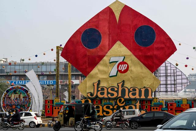 Commuters ride past a large model of a kite celebrating the Basant festival in Lahore on February 3, 2026. (Photo by Arif ALI / AFP)