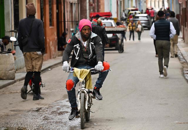 A bundled-up man rides a bicycle down a street in Havana on February 3, 2026. Cuba registered a record low of zero degrees on February 3, 2026, the first time freezing point has been documented on the Caribbean island, according to its Institute of Meteorology. (Photo by YAMIL LAGE / AFP)