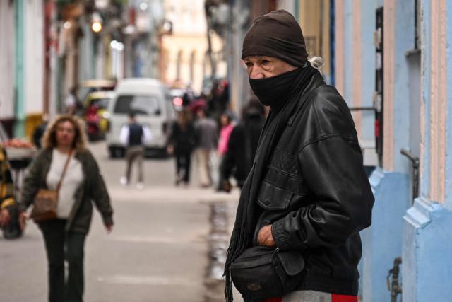 A bundled-up man stands in a street in Havana on February 3, 2026. Cuba registered a record low of zero degrees on February 3, 2026, the first time freezing point has been documented on the Caribbean island, according to its Institute of Meteorology. (Photo by YAMIL LAGE / AFP)