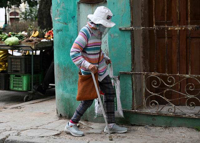 A bundled-up elderly woman walks down a street in Havana on February 3, 2026. Cuba registered a record low of zero degrees on February 3, 2026, the first time freezing point has been documented on the Caribbean island, according to its Institute of Meteorology. (Photo by YAMIL LAGE / AFP)