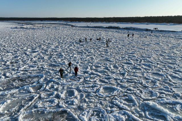 This aerial photograph taken on February 3, 2026 shows people walking on the frozen Baltic Sea near Mikoszewo, northern Poland. (Photo by Sergei GAPON / AFP)