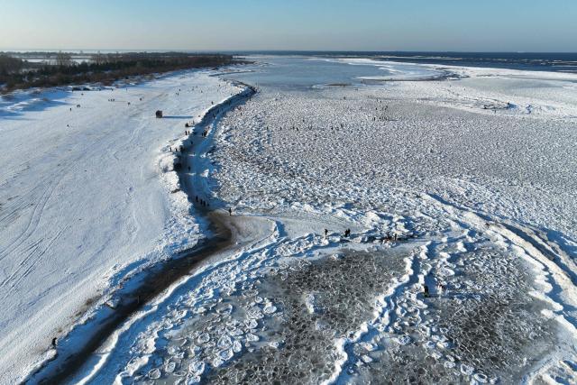 This aerial photograph taken on February 3, 2026 shows people walking along the Baltic Sea beach covered with ice thrown up by the waves as round ice floes float near Mikoszewo, northern Poland. (Photo by Sergei GAPON / AFP)