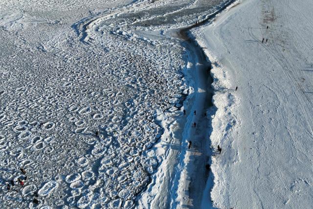 This aerial photograph taken on February 3, 2026 shows people walking along the Baltic Sea beach covered with ice thrown up by the waves as round ice floes float near Mikoszewo, northern Poland. (Photo by Sergei GAPON / AFP)