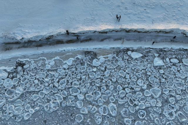 This aerial photograph taken on February 3, 2026 shows people walking along the Baltic Sea beach covered with ice thrown up by the waves as round ice floes float near Mikoszewo, northern Poland. (Photo by Sergei GAPON / AFP)
