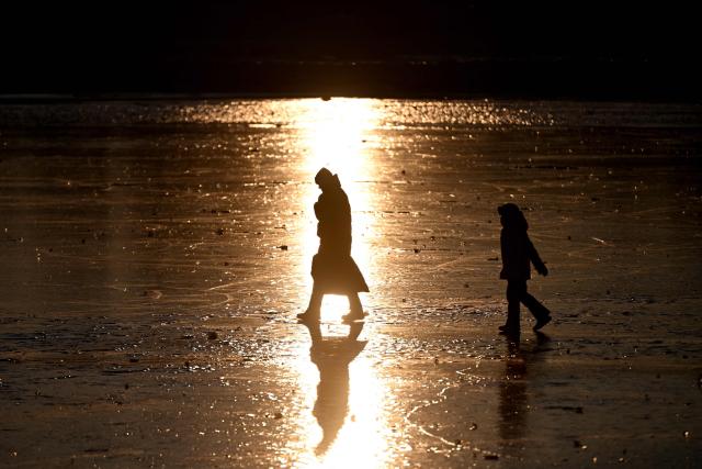 People walk on the relfective surface of the frozen Baltic Sea during sunset near Mikoszewo, northern Poland on February 3, 2026. (Photo by Sergei GAPON / AFP)