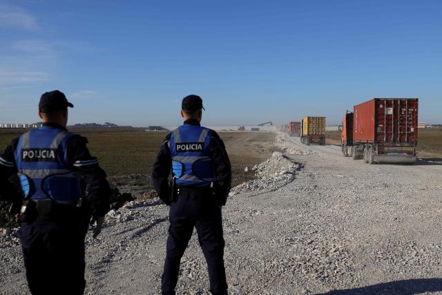 (FILES) Police officers watch as trucks carrying containers of possibly toxic industrial waste enter a controled site after being offloaded from the Turkish-flagged Moliva container ship, in the port of Durres, on November 8, 2024. The Durres Prosecutor's Office issued 33 arrest warrants on February 3, 2026 for suspected involvement in the trafficking of toxic waste that was turned away by Thailand. The waste left the Balkan nation in July 2024 in more than 100 containers. Thailand rejected the consignment following claims by an environmental group that it was illegal toxic waste. The shipment then returned to Albania. (Photo by Adnan Beci / AFP)