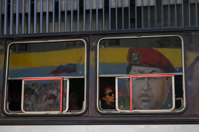 TOPSHOT - A woman travels on a bus as the reflection of a mural depicting late Venezuelan President Hugo Chavez is seen on the window in Caracas on February 3, 2026. (Photo by Federico PARRA / AFP)