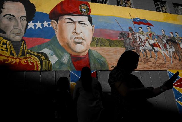 People walk past a mural with the image of the late Venezuelan President Hugo Chavez and Venezuelan liberator Simon Bolivar, outside of the National Assembly in Caracas, on February 3, 2026. (Photo by Federico PARRA / AFP)
