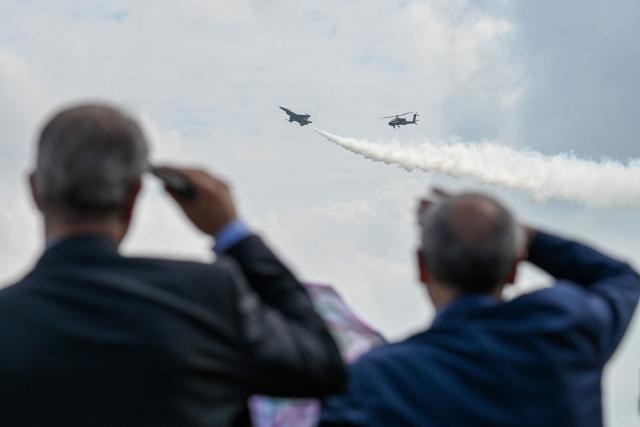 Visitors watch a Republic of Singapore Air Force F-16C fighter jet and AH-64D Apache attack helicopter take part in an aerial display at the Singapore Airshow in Singapore on February 4, 2026. (Photo by Roslan RAHMAN / AFP)