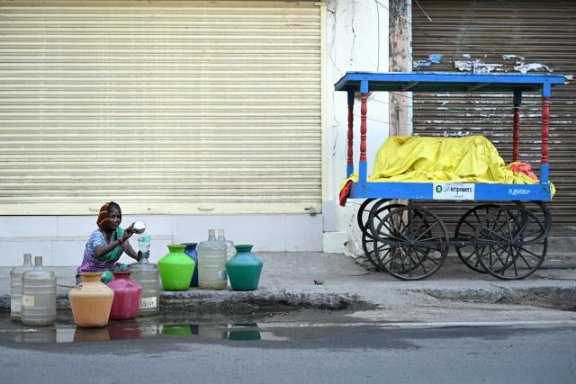 A woman collects water from a leaking pipeline along a street in Chennai on February 4, 2026. (Photo by R.Satish BABU / AFP)