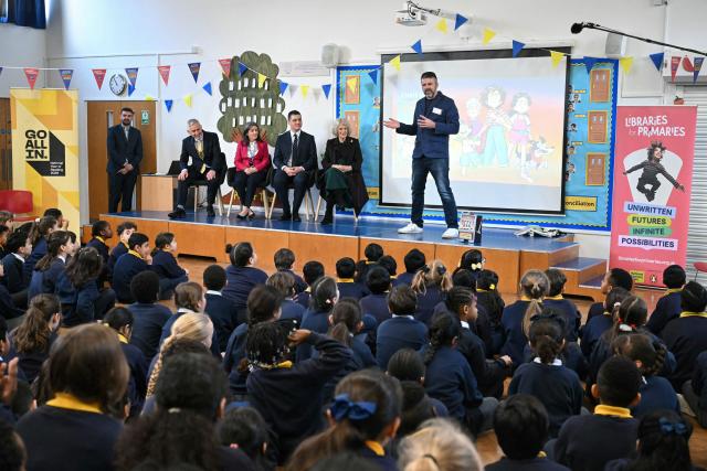 Britain's Queen Camilla (at R-seated on stage) listens to British children's author Chris Smith (R) speak to pupils as she attends the opening of a library at Christ Church Primary School in London on February 4, 2026, to help mark the "National Year of Reading". (Photo by JUSTIN TALLIS / POOL / AFP)