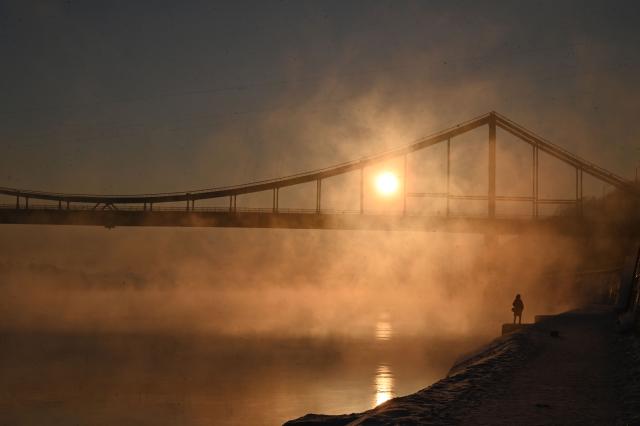 A girl looks at the sun rising over the Dnipro River in Kyiv on February 4, 2026. (Photo by Sergei SUPINSKY / AFP)