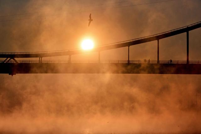 People walk on the pedestrian bridge over the Dnipro River during sunrise in Kyiv on February 4, 2026. (Photo by Sergei SUPINSKY / AFP)