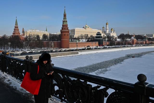 A woman walks along a bridge over the Moskva river, with the Kremlin seen in distance, in central Moscow on February 4, 2026. The Kremlin on February 4, 2026 said it would press on with its almost four-year offensive against Ukraine until Kyiv agrees to Moscow's terms for a settlement, as US-mediated talks opened in Abu Dhabi. (Photo by Hector RETAMAL / AFP)