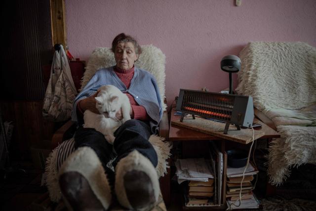 Valentyna Kucherenko, 75, sits with her cat next to an electric heater to warm herself during a heating outage following Russian strikes in Kharkiv on February 4, 2026, amid the Russian invasion of Ukraine. Recent Russian strikes on Ukraine's power infrastructure have disrupted light, heating and water supplies to millions across the country as temperatures plummet well below freezing, leaving the war-battered country facing a fresh humanitarian crisis. (Photo by Ivan SAMOILOV / AFP)