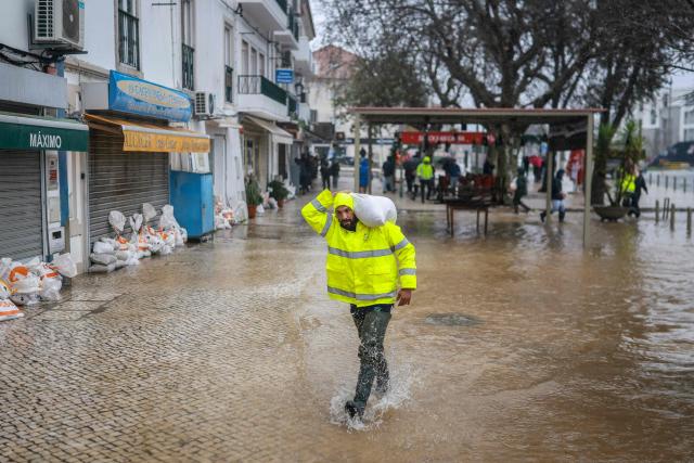 A man carries a sandbag to protect building entrances as floodwaters from Sado River cover the street in Alcacer do Sal, south of Portugal, amid Storm Leonardo on February 4, 2026. A storm unleashing up to 35 centimetres (14 inches) of rain in 24 hours battered the Iberian Peninsula today, forcing thousands of people in southern Spain from their homes, shutting schools and cancelling trains. Leonardo compounded difficulties for residents in Portugal who were already reeling from last week's Storm Kristin, which killed five people, injured hundreds and cut off tens of thousands of customers from the power grid. (Photo by PATRICIA DE MELO MOREIRA / AFP)
